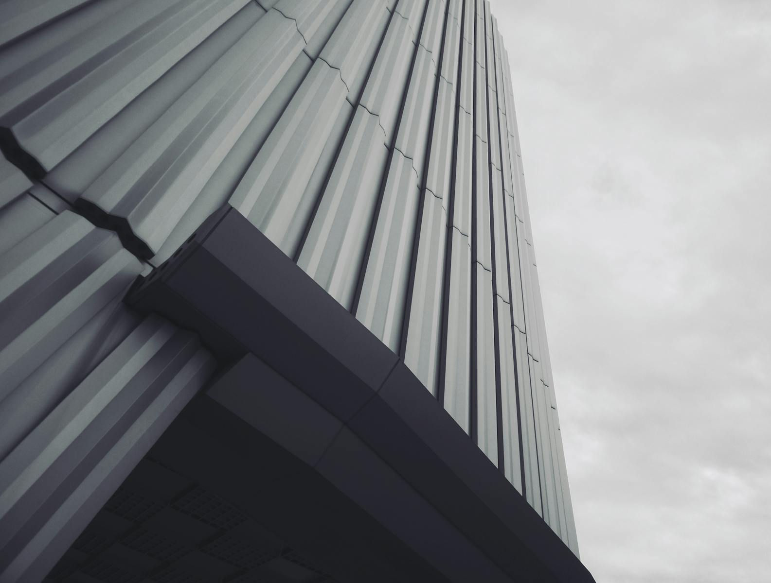 Low angle shot of a modern building with gray tones and overcast sky, emphasizing architectural lines.