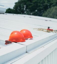 Red hard hats and safety equipment on a metal roof, emphasizing construction safety. {{brizy_dc_image_alt imageSrc=