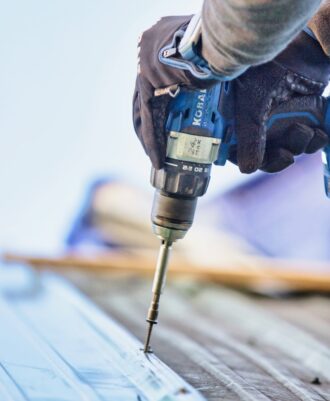 A person using a drill to fasten a piece of metal roofing
